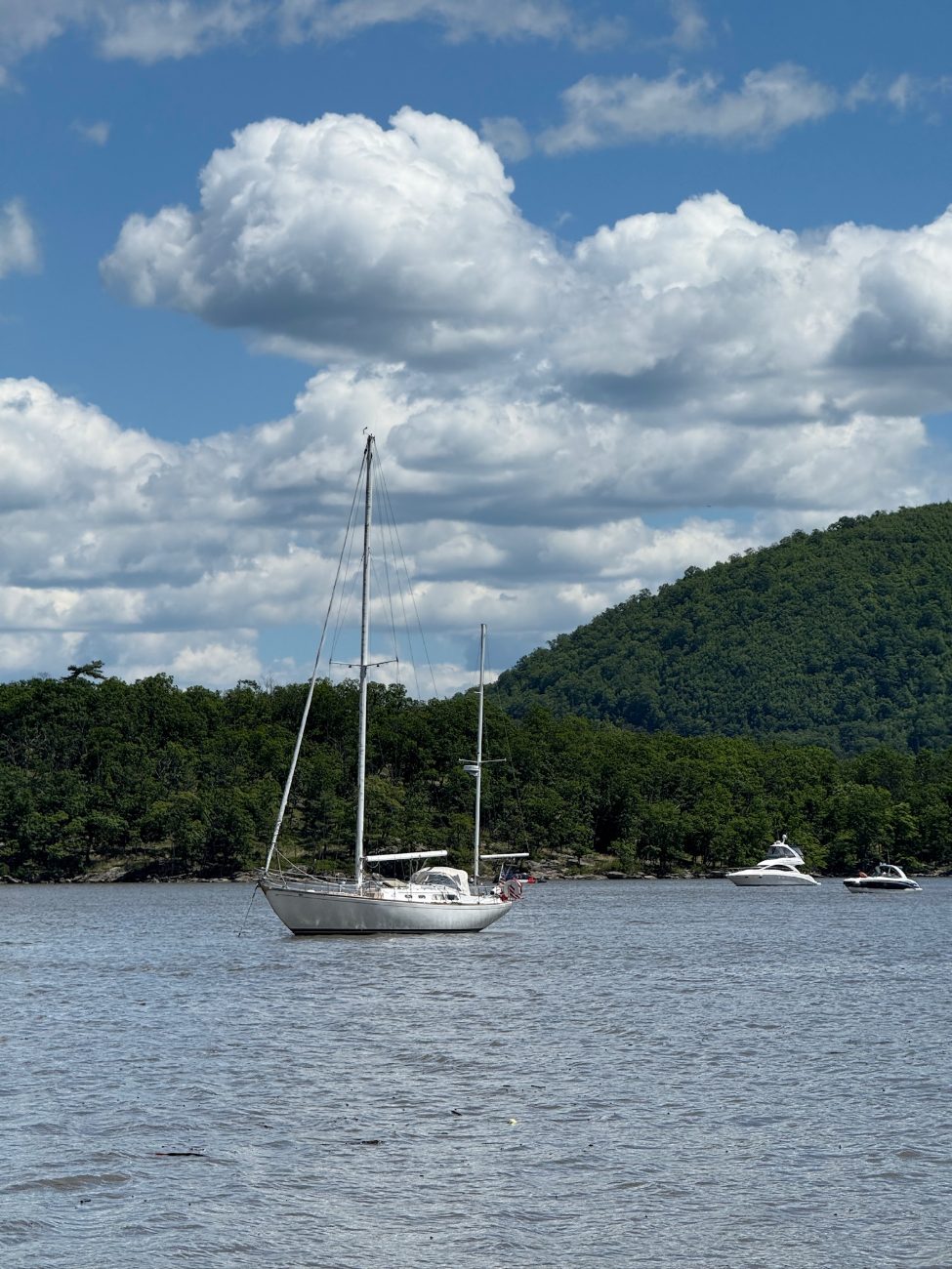 A sailboat at anchor beneath wooded hills